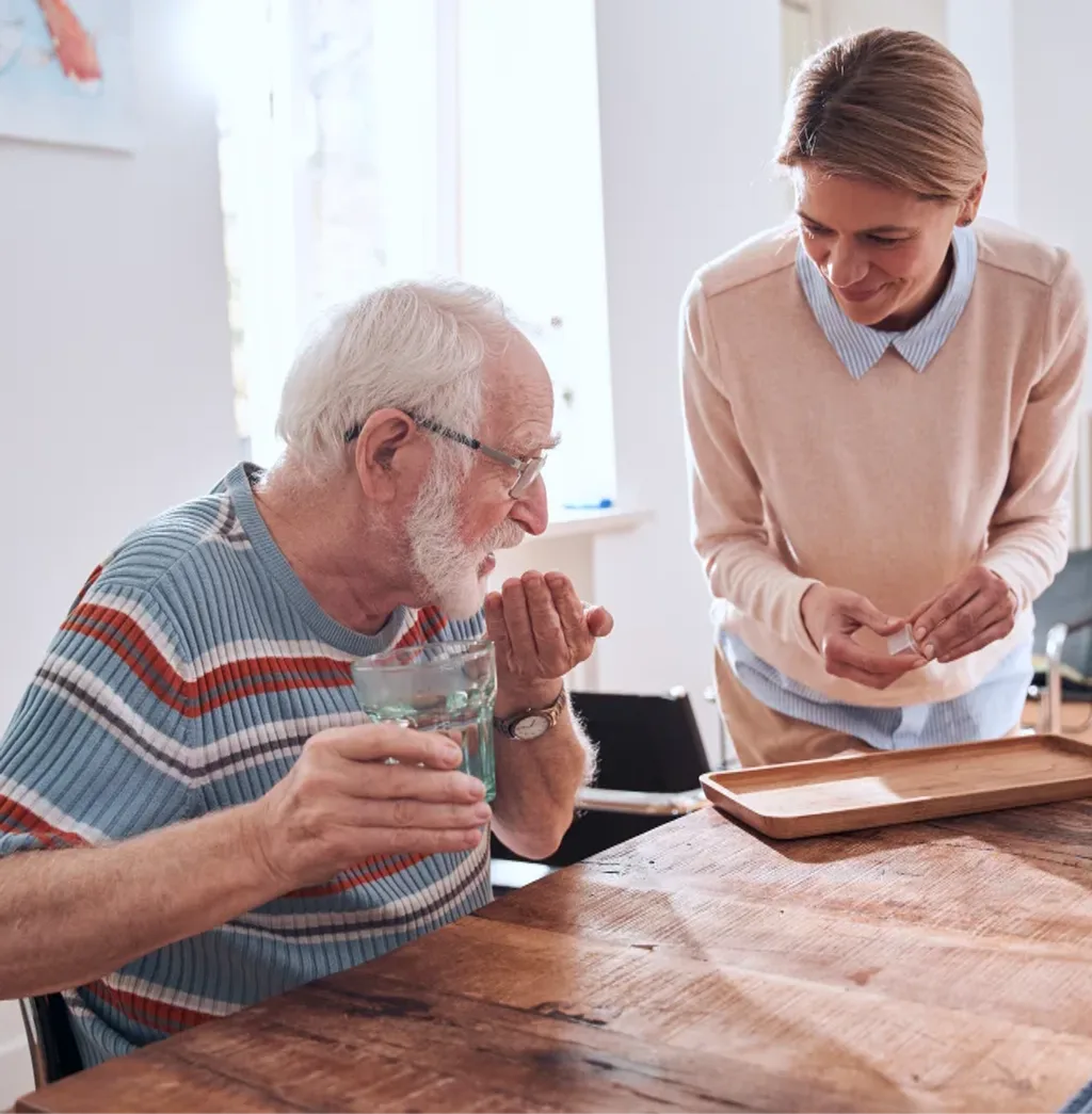 Caregiver helping elderly man with medication